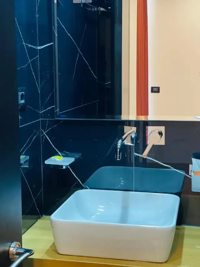 A bathroom lined in black veined marble with a bath and a wall-mounted mixer