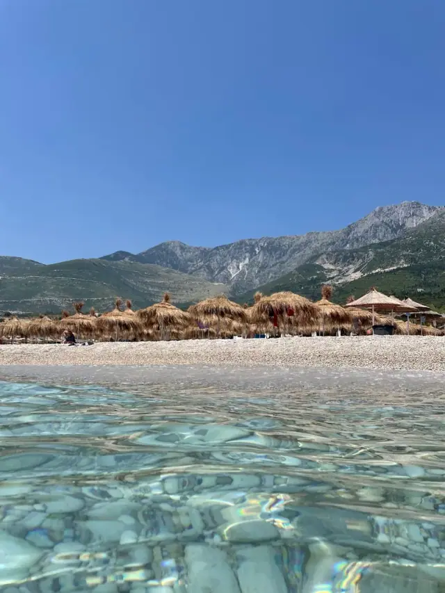 Clear shallow water and umbrellas at Drymades with the mountains behind