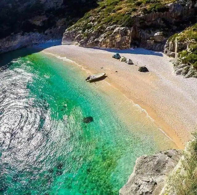 Aerial of Grama Bay's white pebble strand with a boat pulled up and tents behind