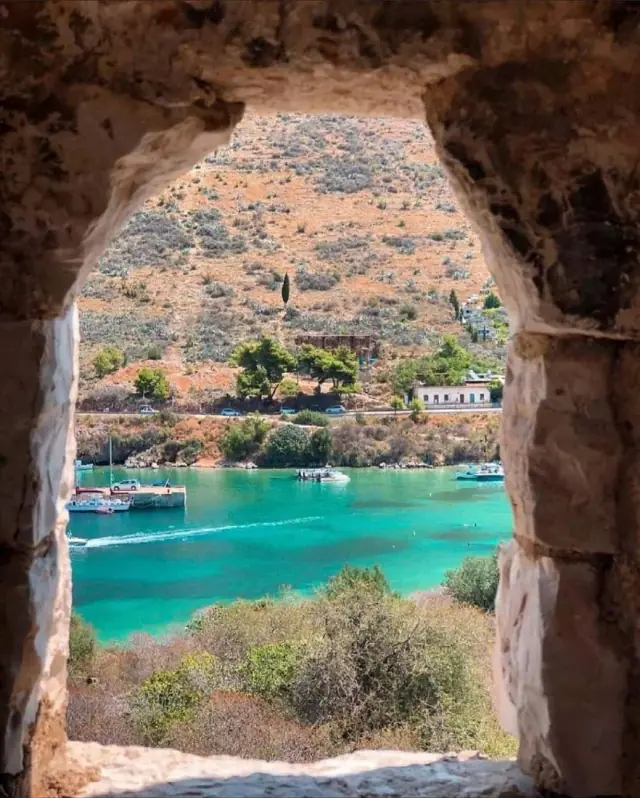Porto Palermo bay framed by a stone arch, boats on turquoise water