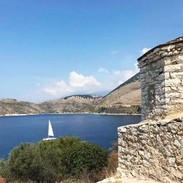 The castle wall above Porto Palermo bay with a sailboat beyond