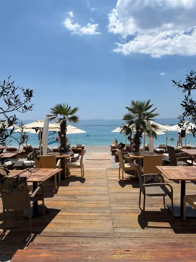 Wooden beach deck with tables leading to the turquoise sea at Aloni Restaurant in Dhërmi