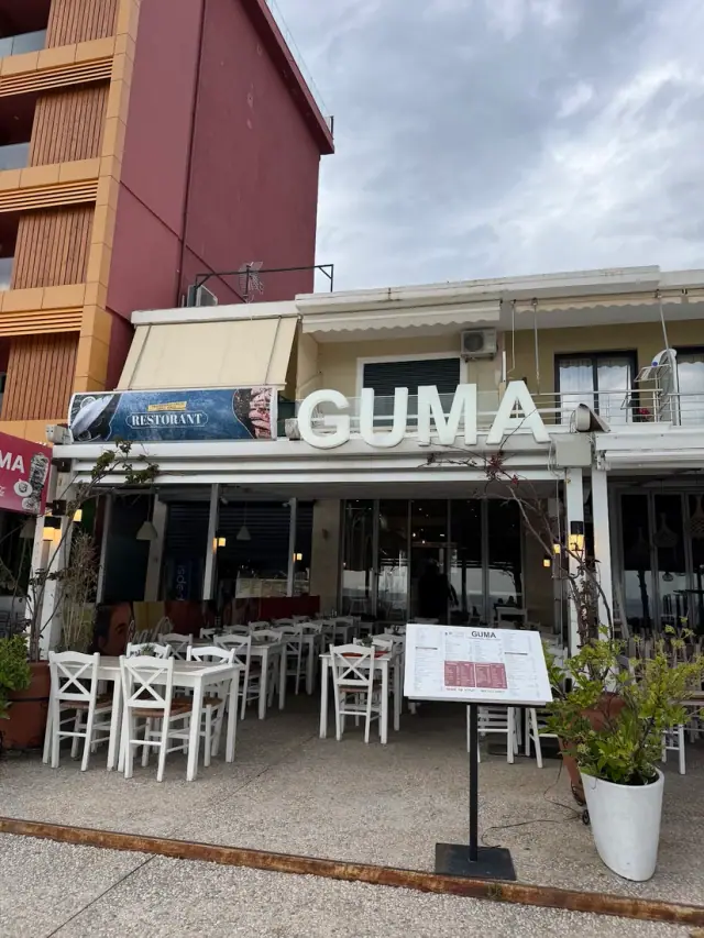 Street-front storefront with the GUMA sign and white outdoor chairs at Guma Restorant in Himara