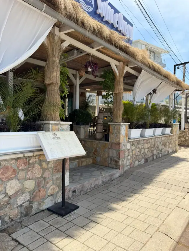 Thatched-roof street terrace and menu board outside LaMer Restaurant in Himara