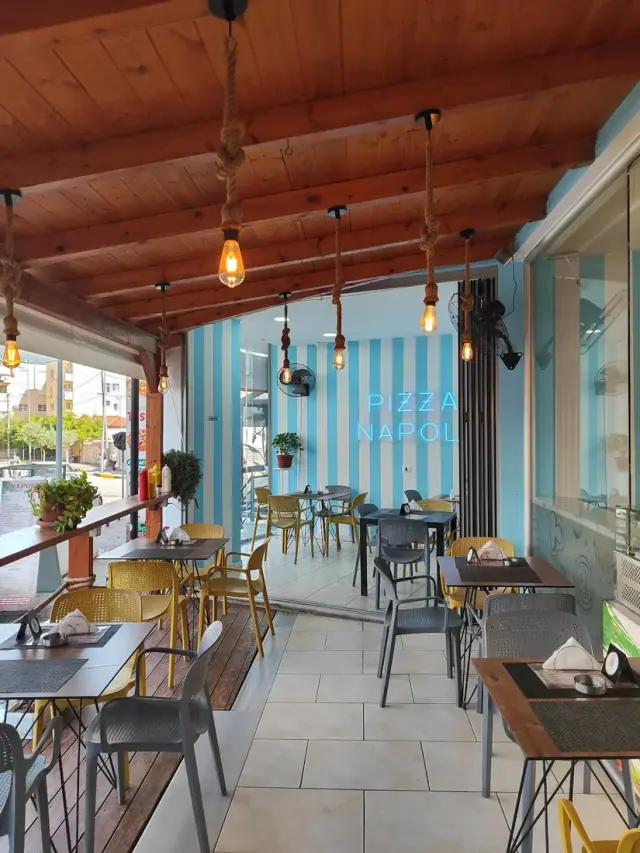 Covered terrace with the Pizza Napoli neon sign on a striped blue wall in Himara