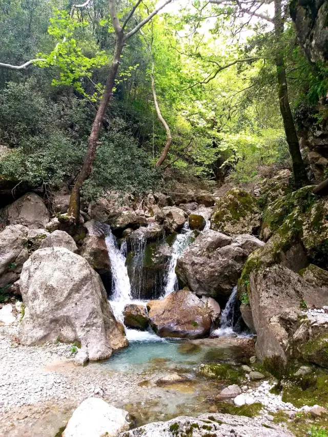 Vuno Waterfall spilling over mossy boulders in a wooded gorge