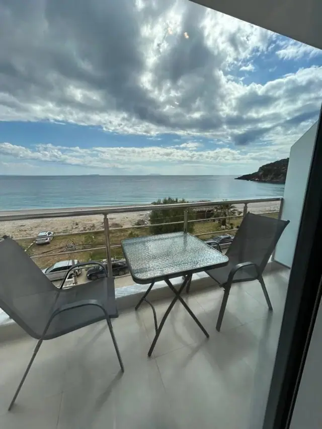 A balcony table and chairs at Ionian View, looking across the beach road to Livadhi bay curving away towards the headland