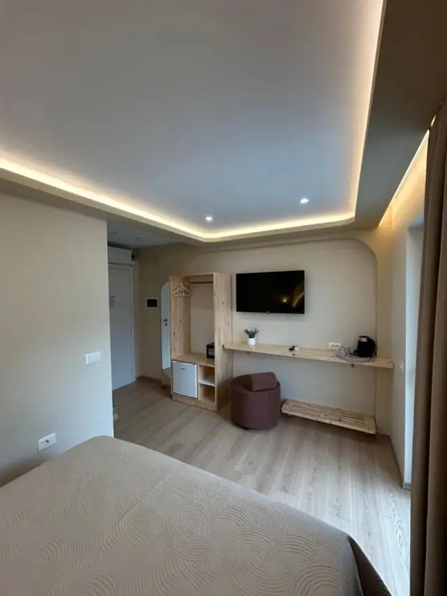 A room with a timber shelf and desk along the wall beneath a wall-mounted television, an arched niche beside it
