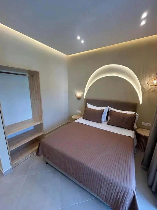 A double room with a domed arc of concealed light above the bed and an open timber wardrobe to the left