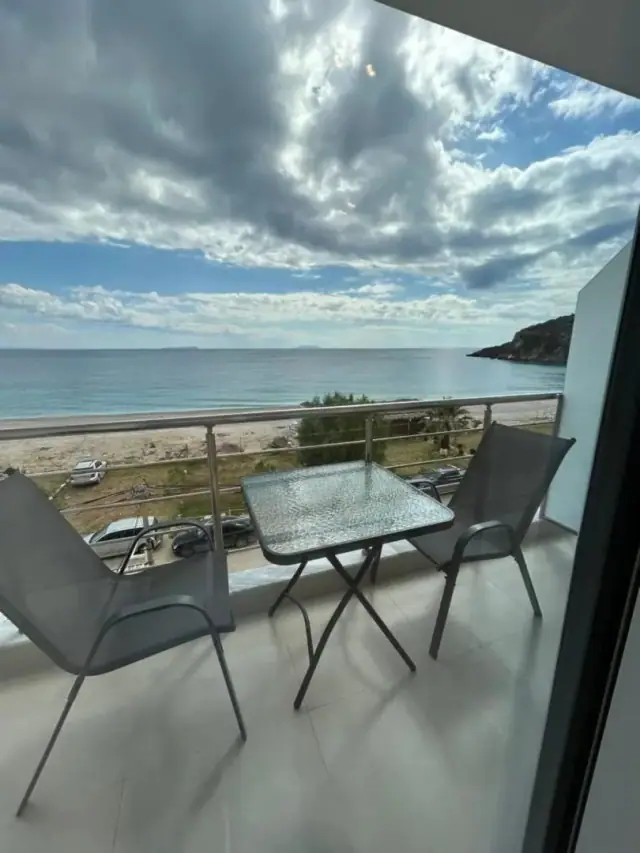 A balcony table and chairs above Livadhi Beach, the bay curving away towards the headland