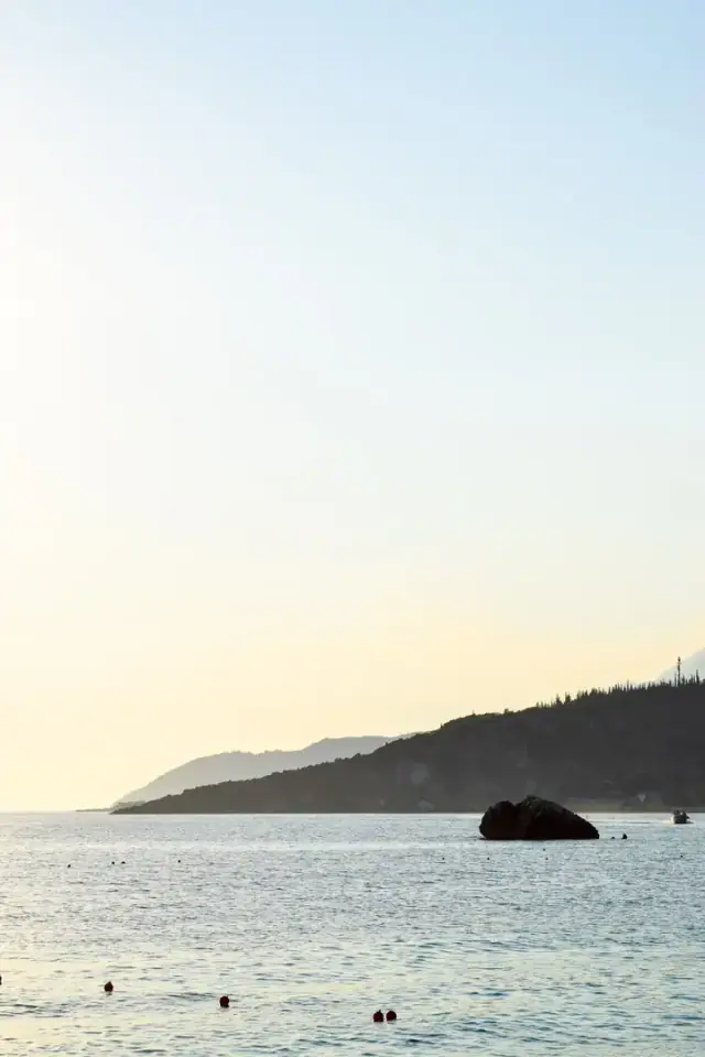 The bay at Livadh from the water's edge, with the offshore rock and the wooded headland beyond