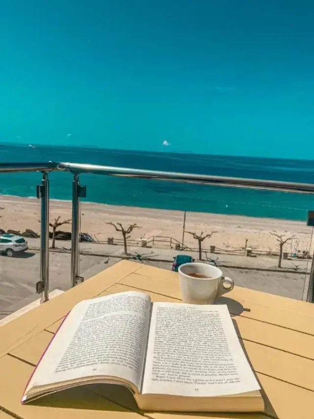 An open book and a cup of coffee on a balcony table at Kleanthi's Hotel above the beach