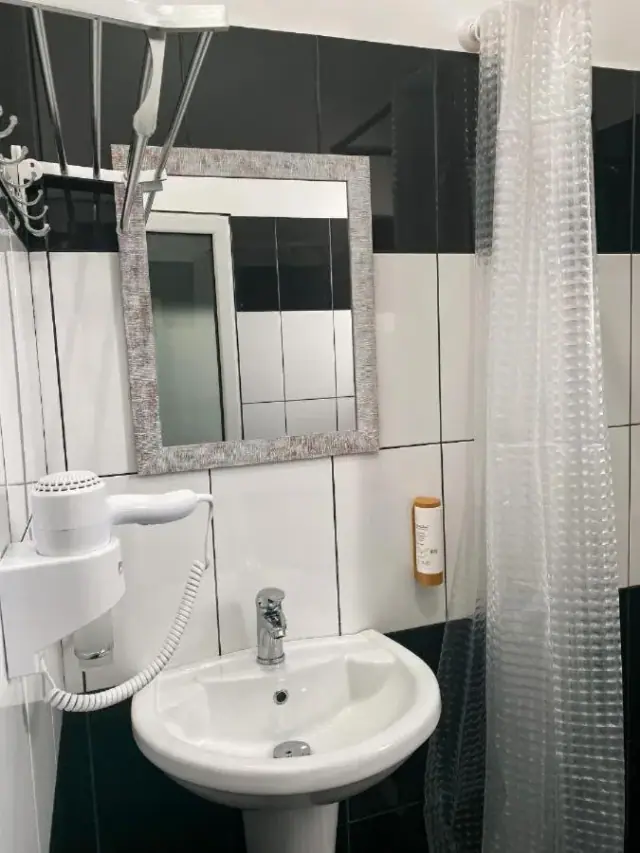 A private bathroom at Kleanthi's Hotel tiled in black and white, with a mirror, hairdryer and shower