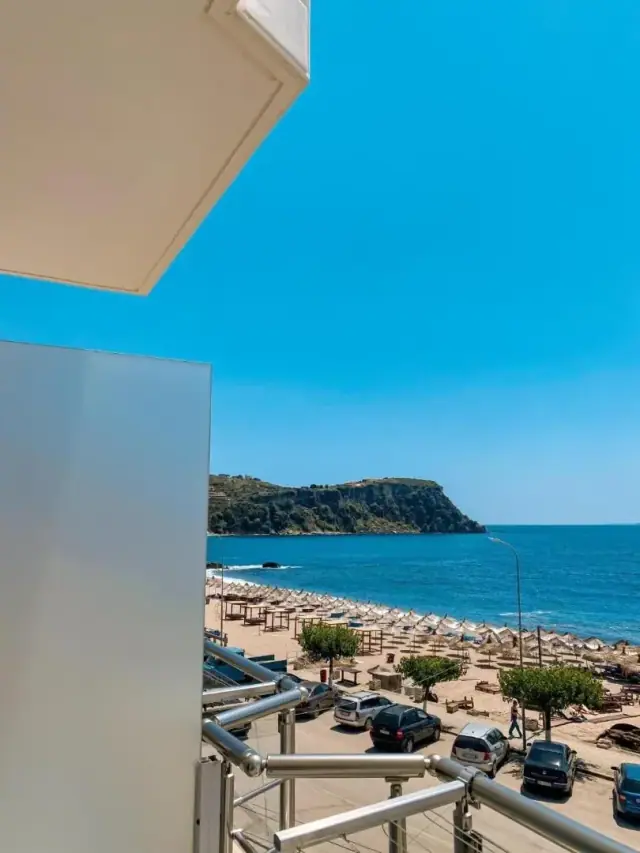 The view from a balcony at Kleanthi's Hotel past a frosted privacy screen to Prinos Beach, its straw parasols and the headland beyond