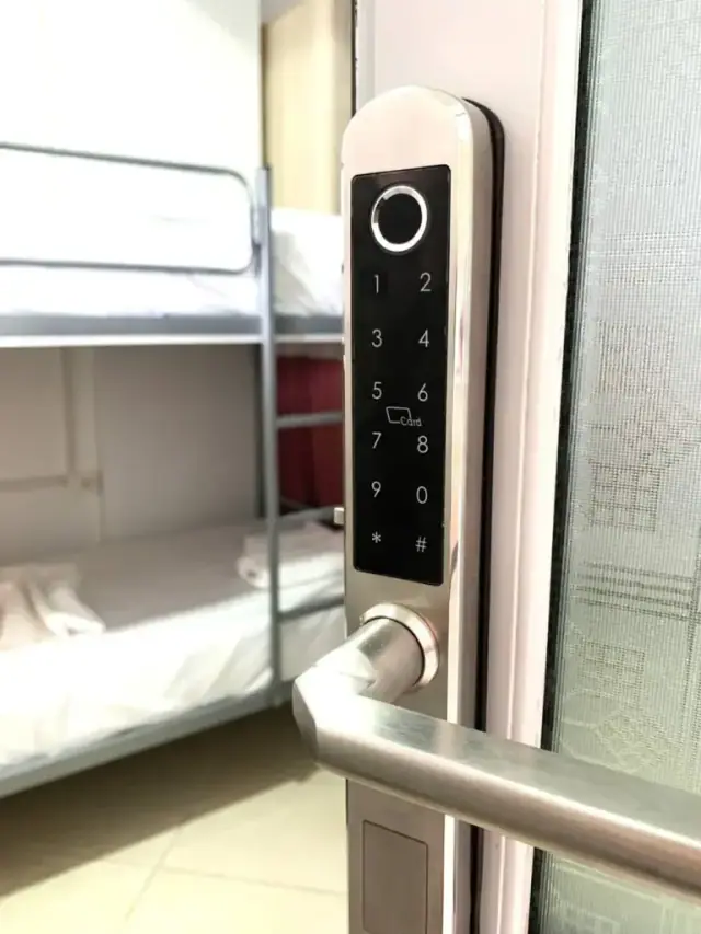 A steel door handle with a keypad and card-reader entry panel, a dormitory with bunk beds visible through the open door