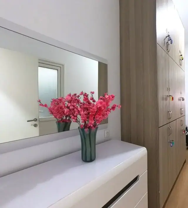 A long mirror over a white chest of drawers with a vase of pink blossom, beside a wall of wooden lockers with coloured key fobs in the doors