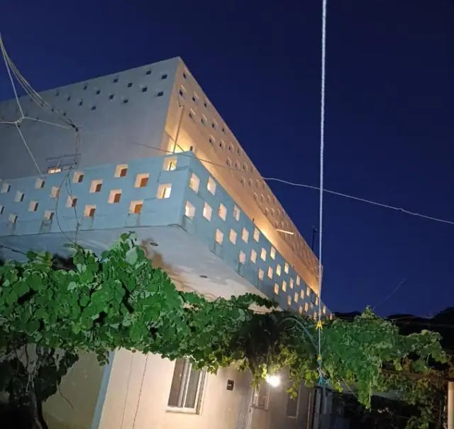 The house at Nikolari Resorts after dark, its upper storeys made of concrete blocks pierced with square holes that glow warm from the lamps inside, a grapevine spread over the terrace below