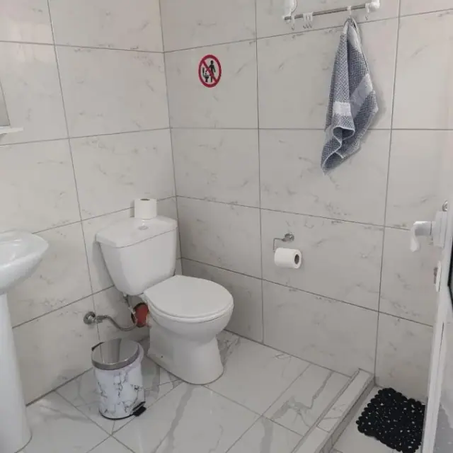 The private shower room of an apartment at Nikolari Resorts, marbled white tiles floor to ceiling, a corner shower tray and a folded grey towel on the rail