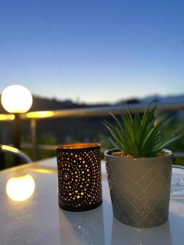 A pierced metal lantern and a potted succulent on a white terrace table against a deep blue evening sky