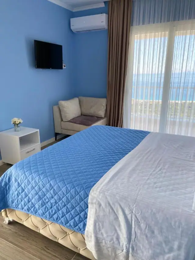 A room with blue walls and a blue bedspread, a pale sofa, and a window with the sea in it
