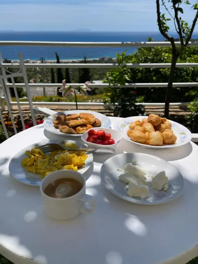 Plates of pastries, strawberries, scrambled eggs and white cheese laid out on a table by a garden rail
