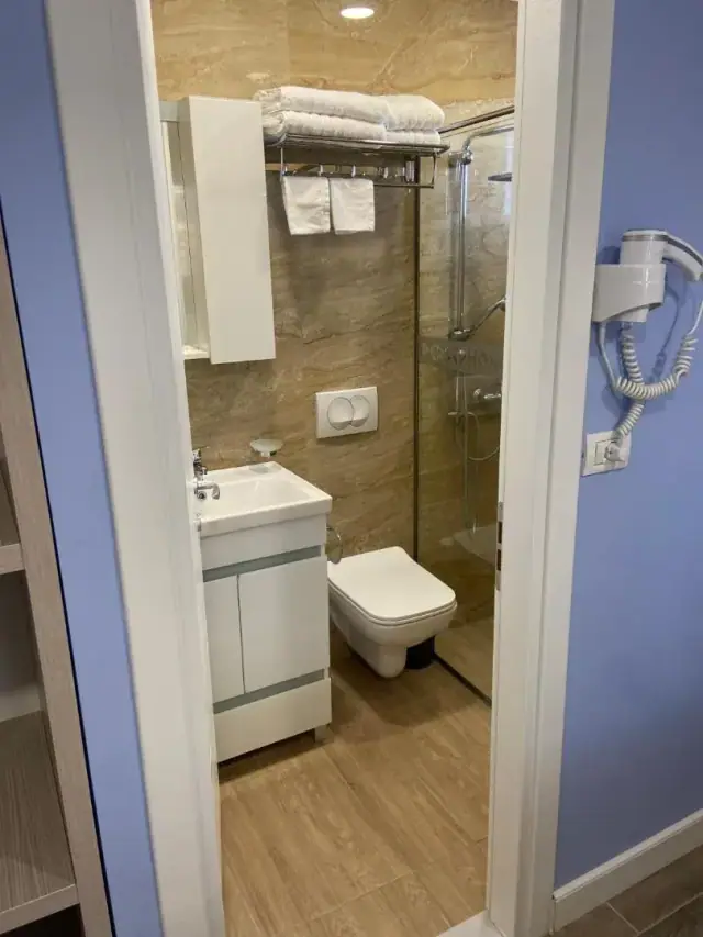 A bathroom with a basin, a wall-hung lavatory and a glazed shower lined in tan marble