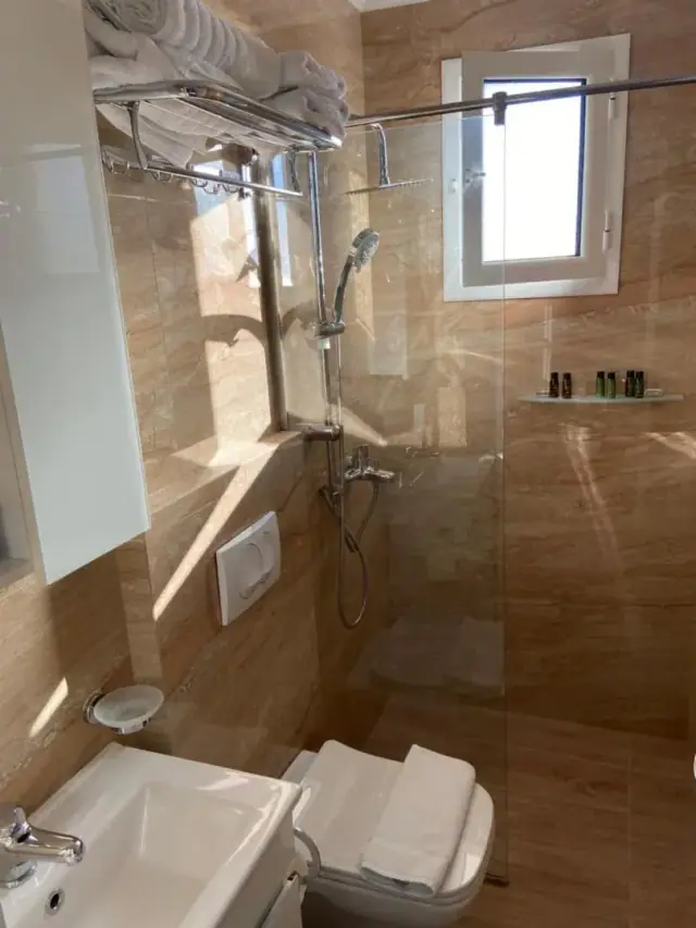 A walk-in shower lined floor to ceiling in tan marble behind a glass screen