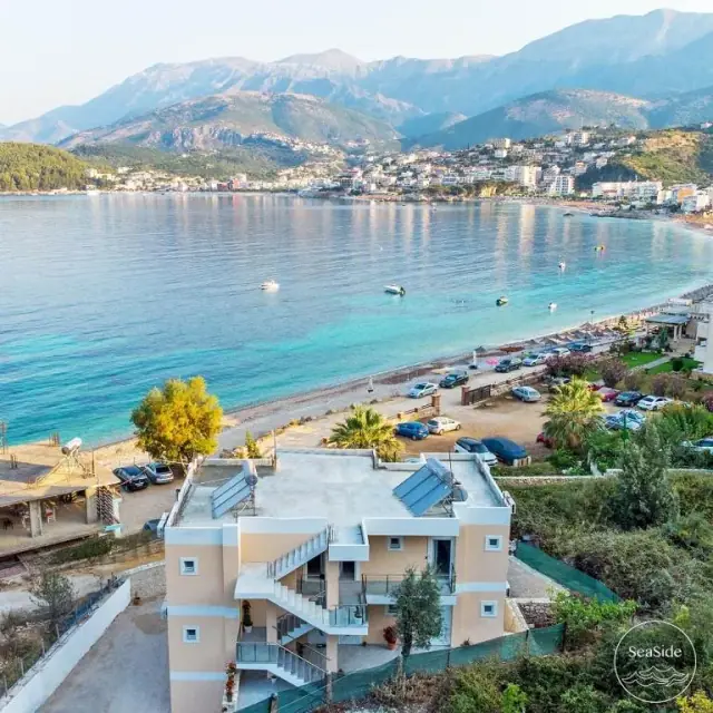 Potam bay from the hillside above Seaside Hotel: the hotel's roof and outside stair, the beachfront car park, the beach, and Himarë across the water