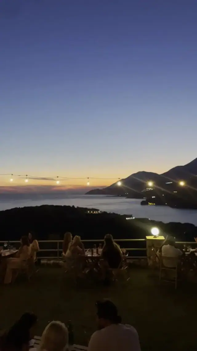 The bay at dusk from the terrace, lamps lit and the coastline fading to silhouette