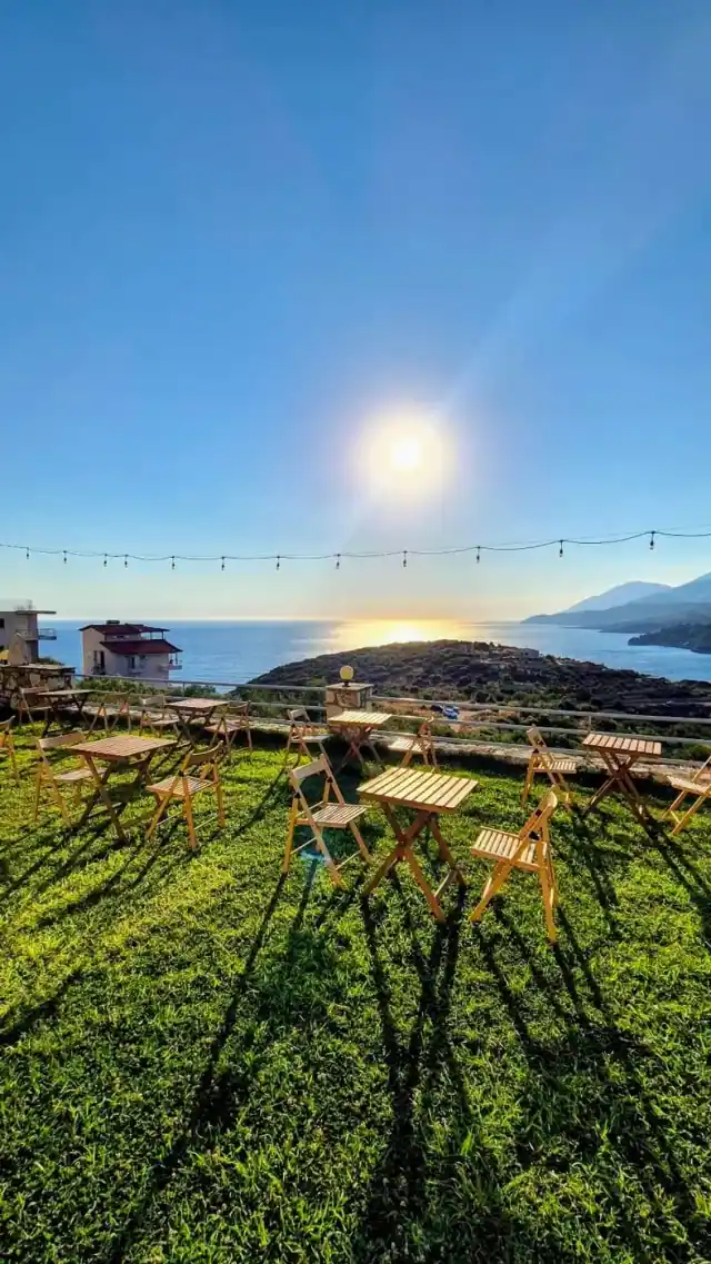 Empty folding wooden tables and chairs on a mown lawn with festoon lights and the bay beyond
