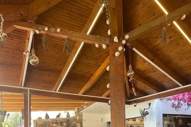 The pitched timber roof of the dining room at Taverna Velco, hung with bunches of dried herbs, strings of seashells and filament bulbs