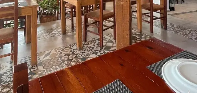 Wooden tables and chairs on a patterned grey and white tile floor in the dining room at Taverna Velco