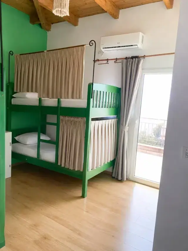 Green bunk beds with an air-conditioning unit and a balcony door letting in daylight