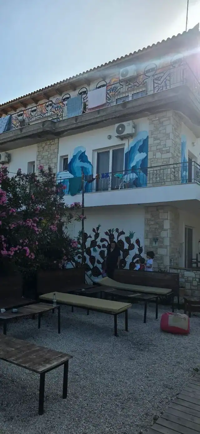 The side of the villa painted with blue figures and a cactus mural, with benches on the gravel