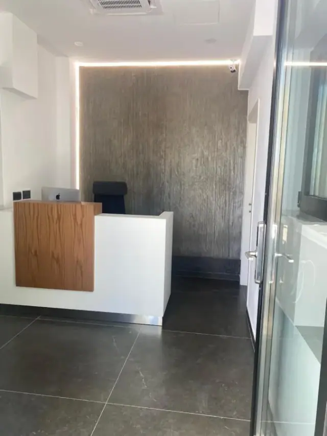 The small reception desk in pale timber and white against a dark textured wall