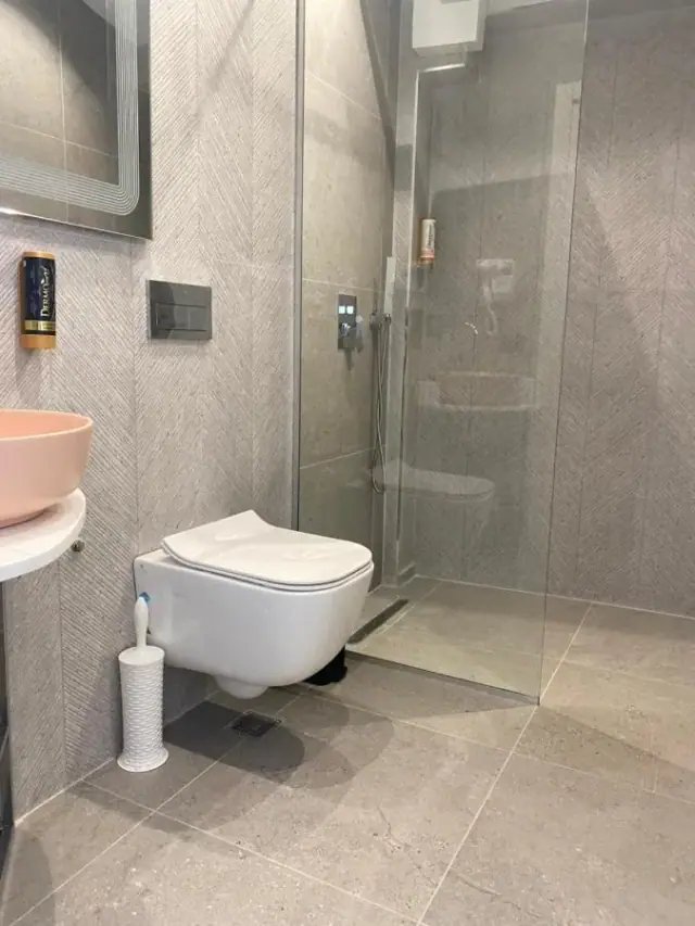 A grey stone-tiled bathroom with a wall-hung toilet and a walk-in shower