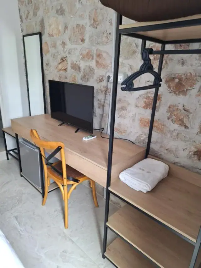 A timber desk and open clothes rail against the exposed stone wall, a folded towel carrying the house monogram