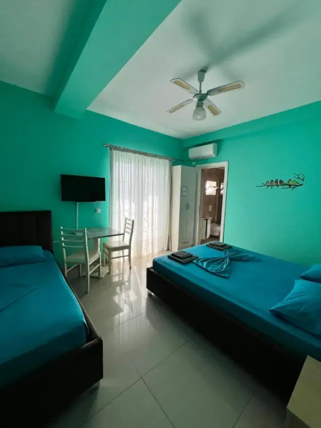 A room painted turquoise with a bed, a small table and chairs, a wall-mounted television and an air conditioner