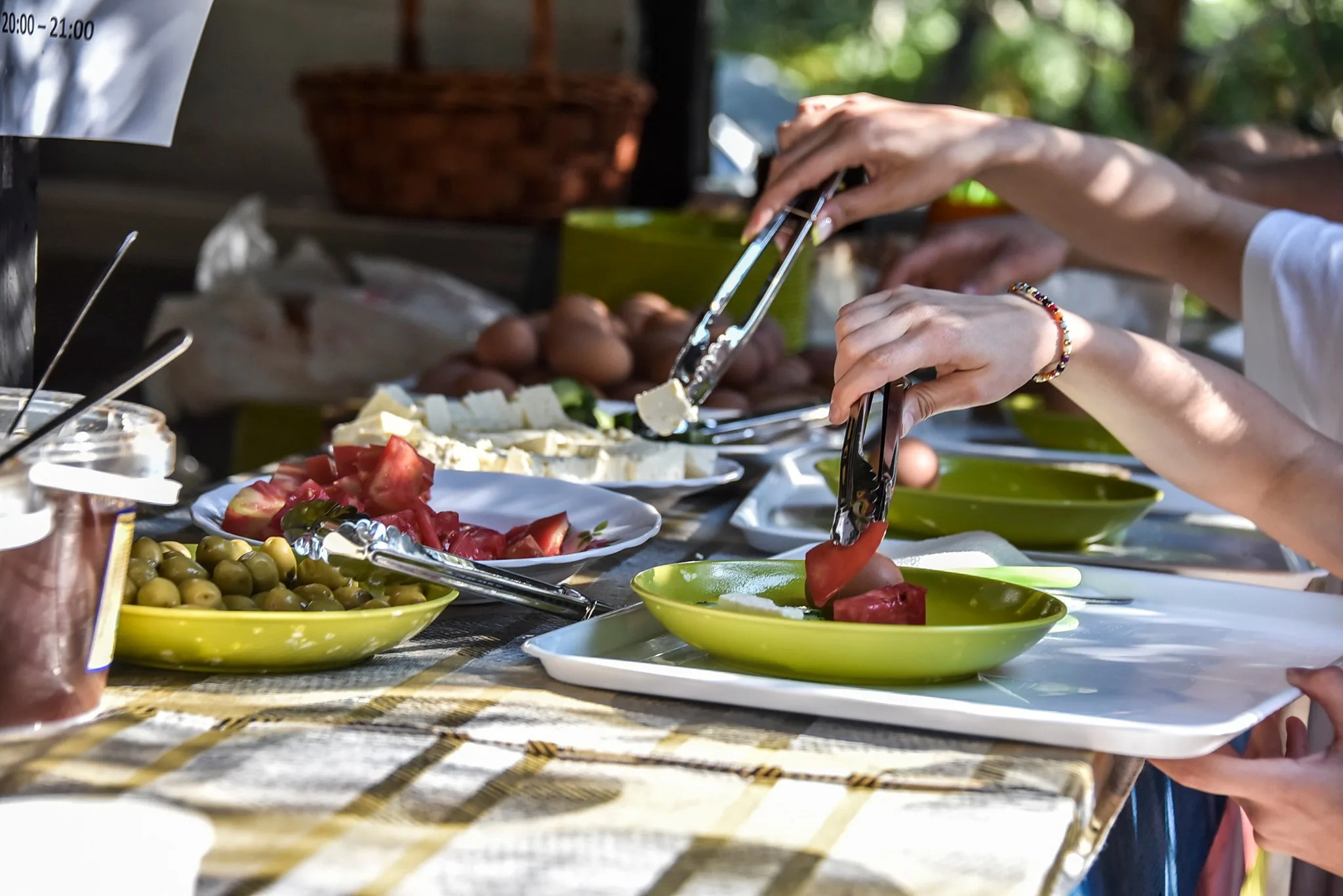 Hands serving tomatoes, cheese and olives from a breakfast table onto green plates and white trays