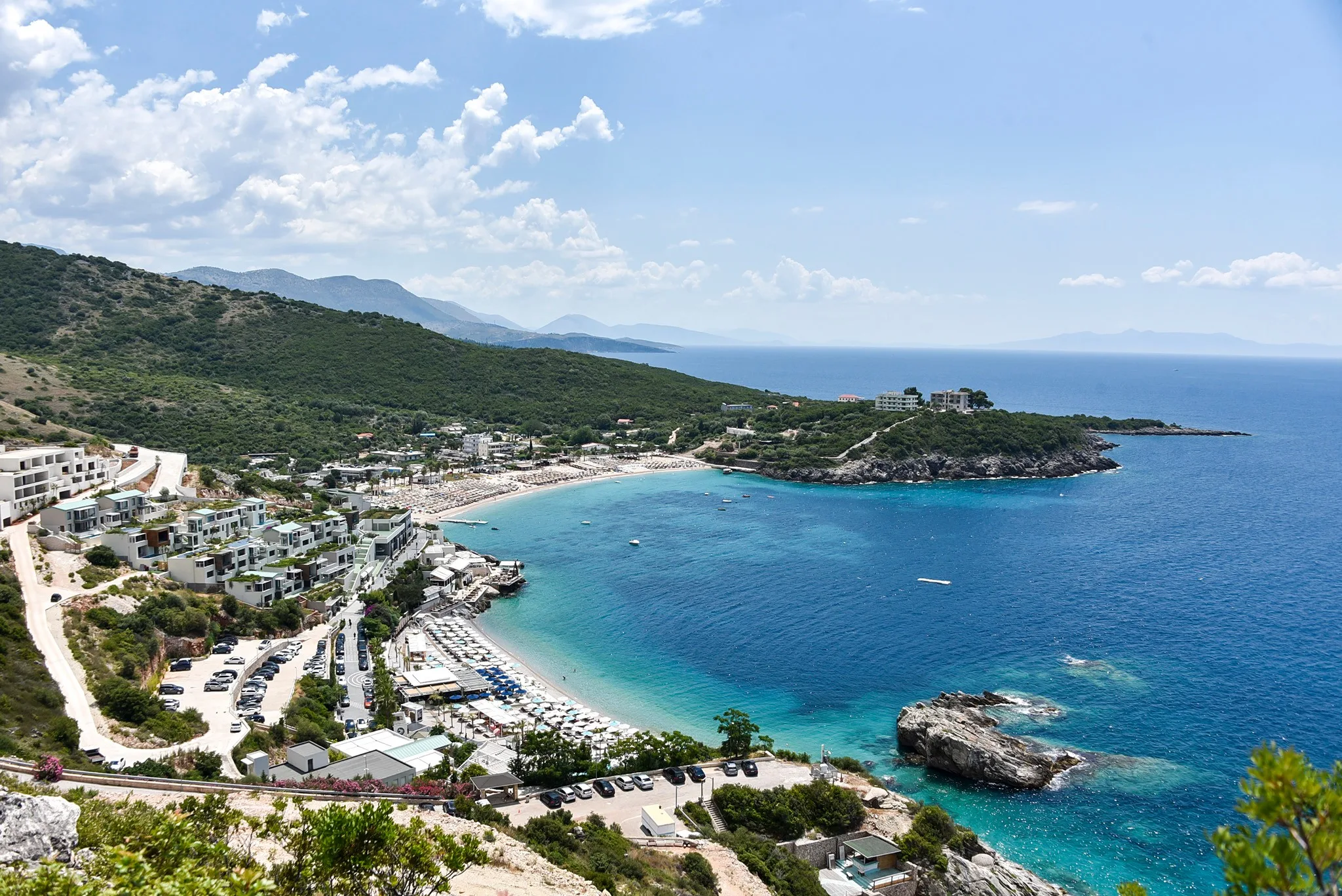 Jalë bay from the hillside above: a pale beach, turquoise water and a wooded headland