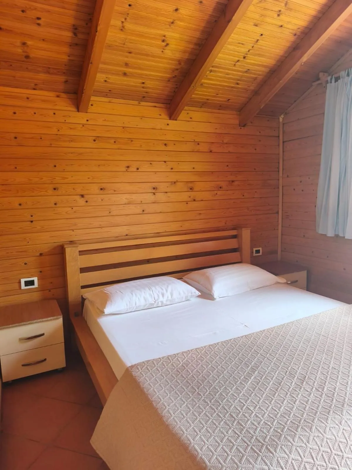 A double bed with white pillows and a pine headboard in a pine-boarded bungalow bedroom