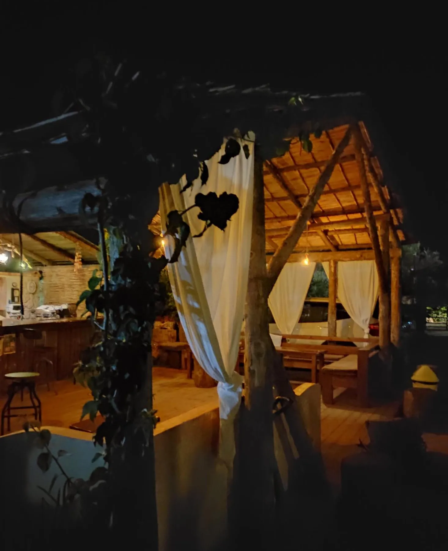 The bar counter and tables seen between white curtains and a vine at night