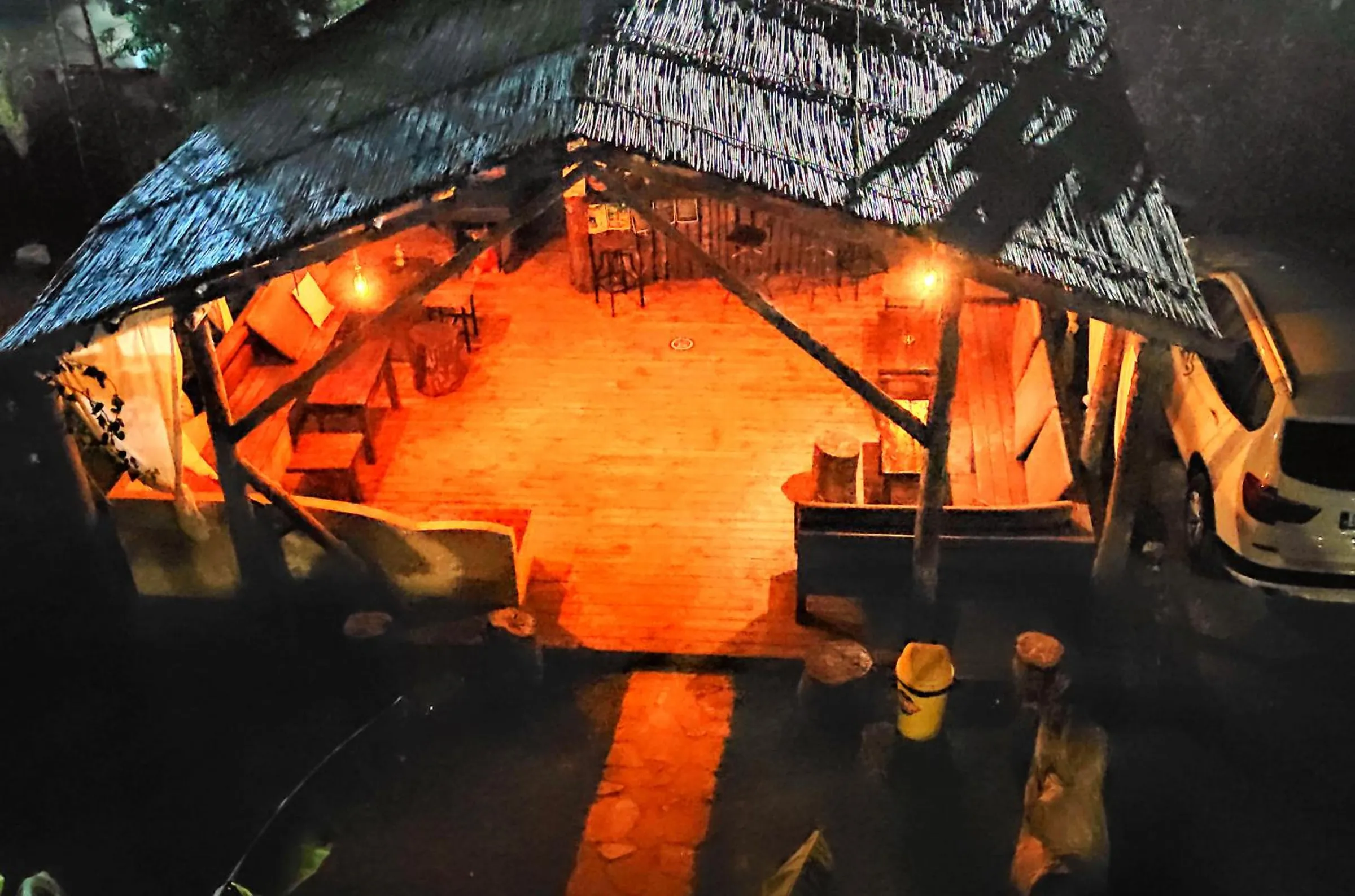The thatched pavilion from above at night, its plank floor and benches lit orange