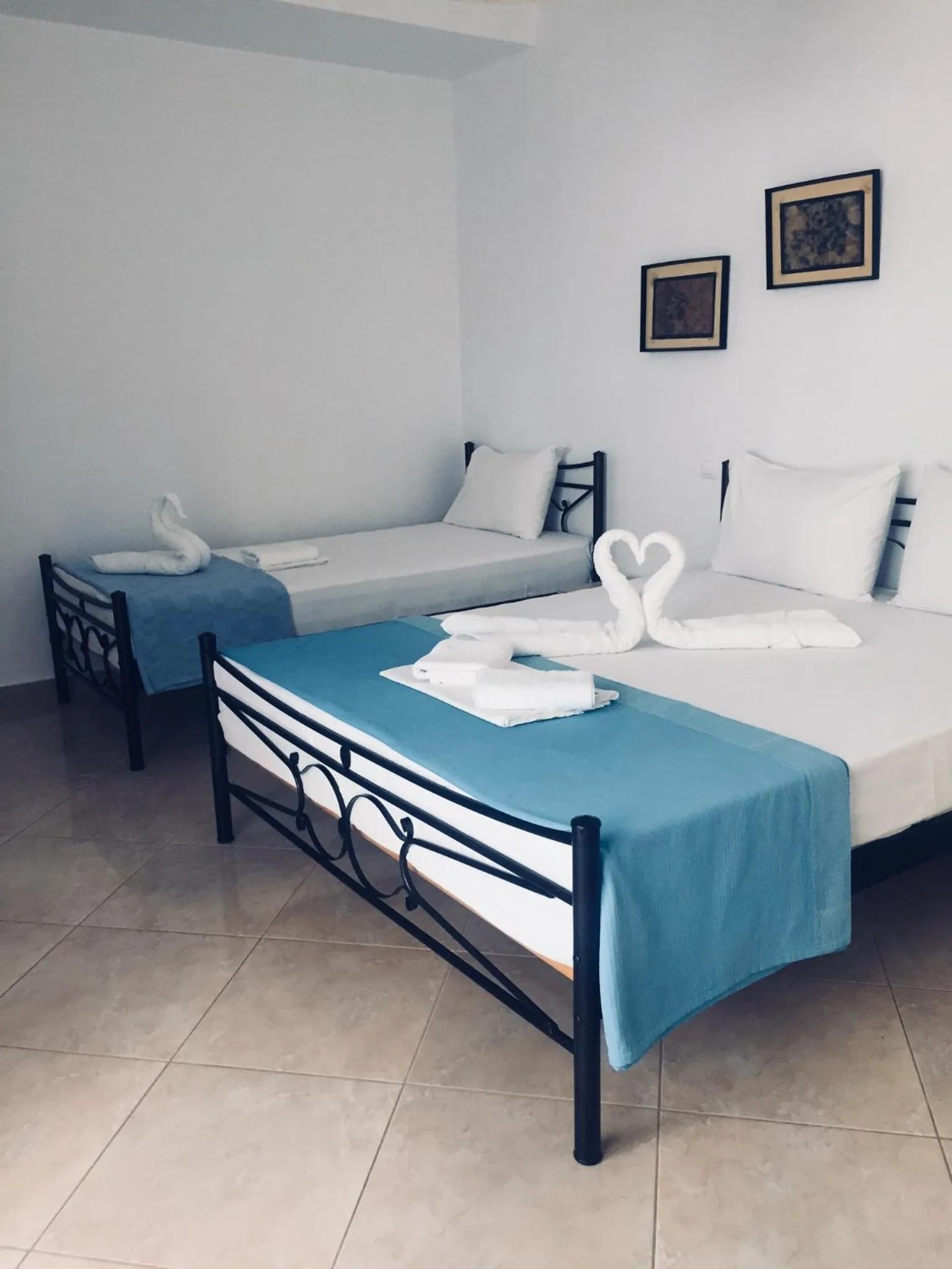A white room with a double and a single wrought-iron bed under teal throws, towel swans on the double, two small framed prints on the wall