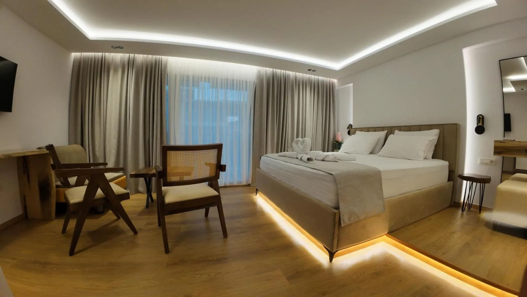 A newer room with an oak floor, a lit cove ceiling, a double bed on an upholstered base, two cane armchairs and full-height curtains
