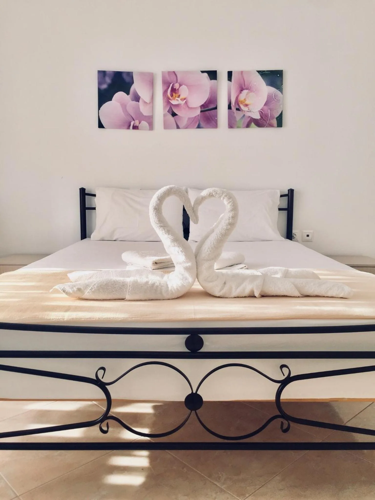 A double bed with a scrolled wrought-iron foot, towel swans on a cream throw and three orchid prints above it