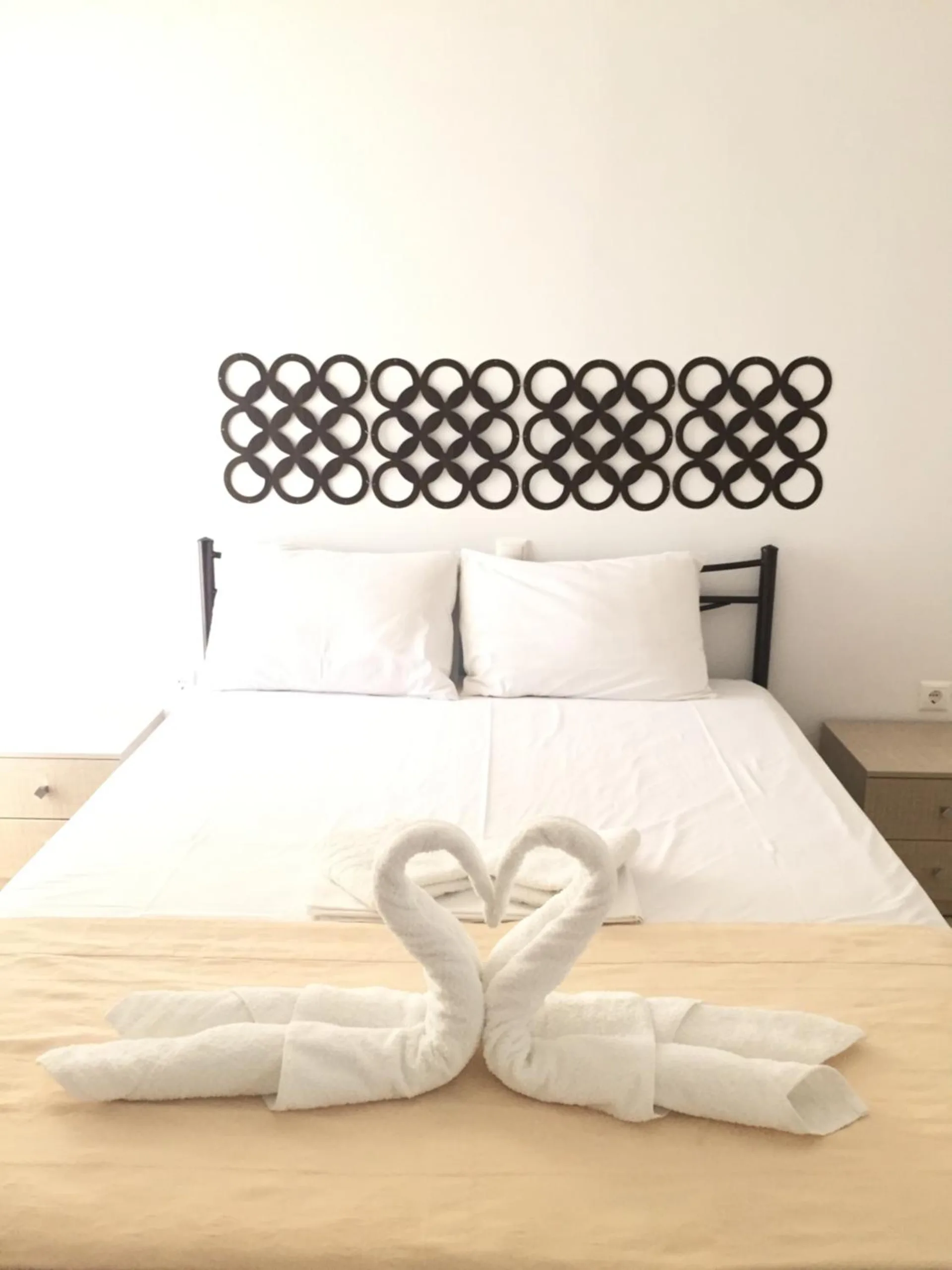 A double bed made up in white with towel swans, under a dark wall panel of interlocking rings