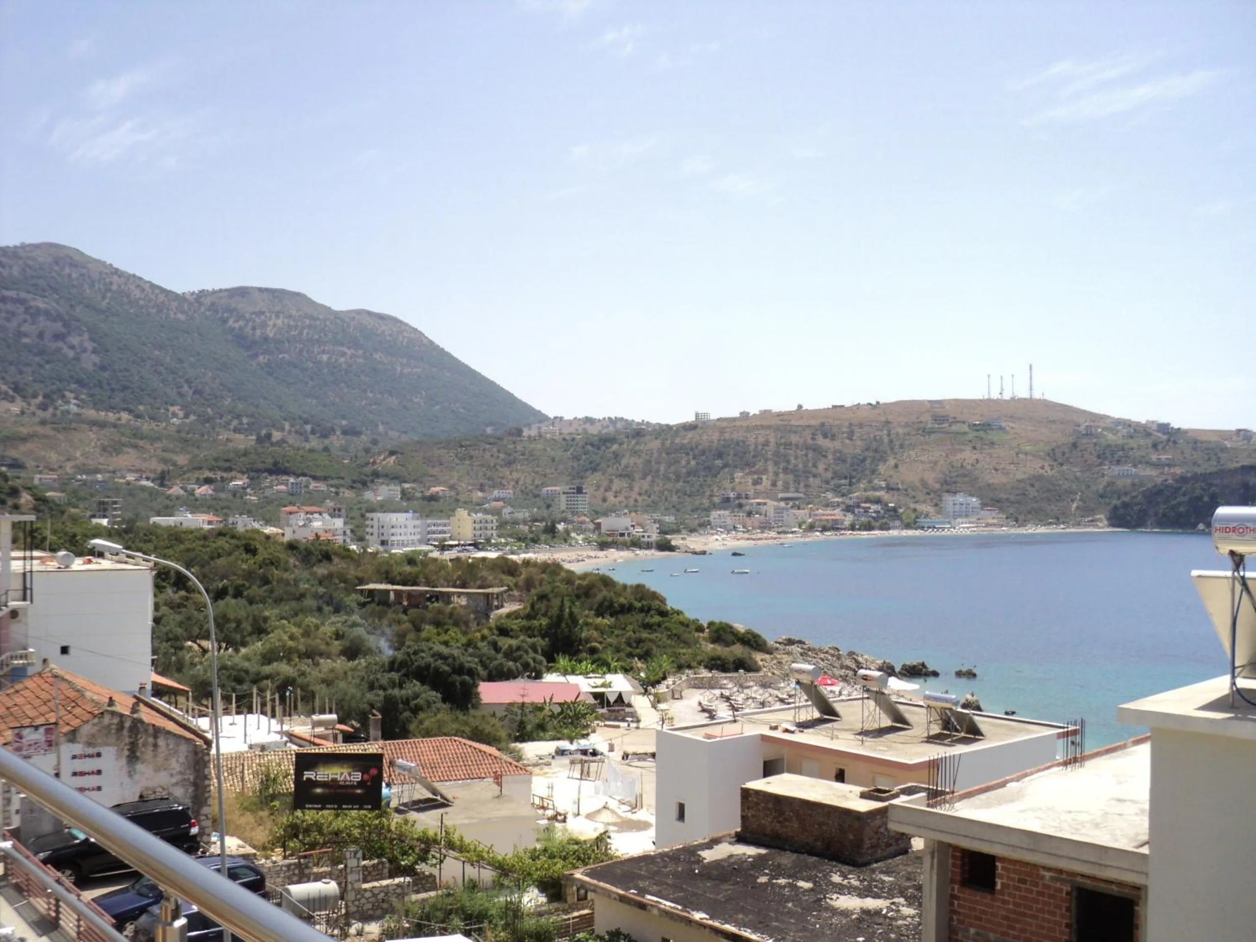 The view from the roof over the houses below to the long curve of the bay and the mountains behind Himarë