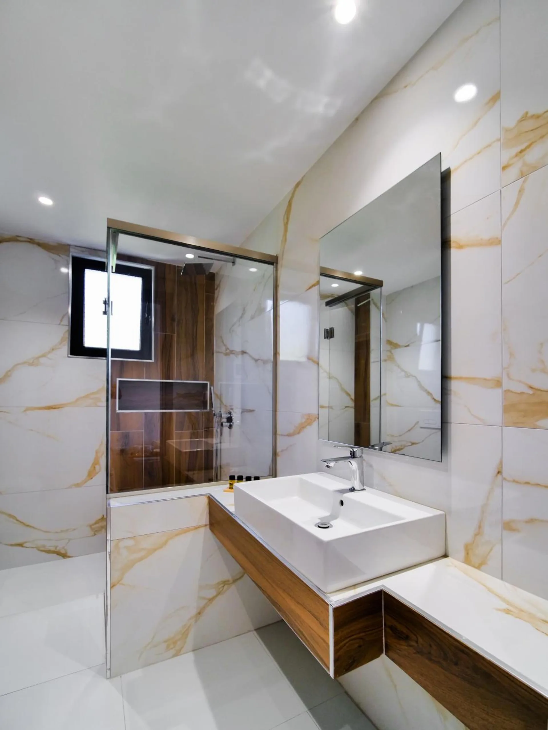 A bathroom in gold-veined white marble, a walk-in glass shower, a vessel basin on a walnut shelf