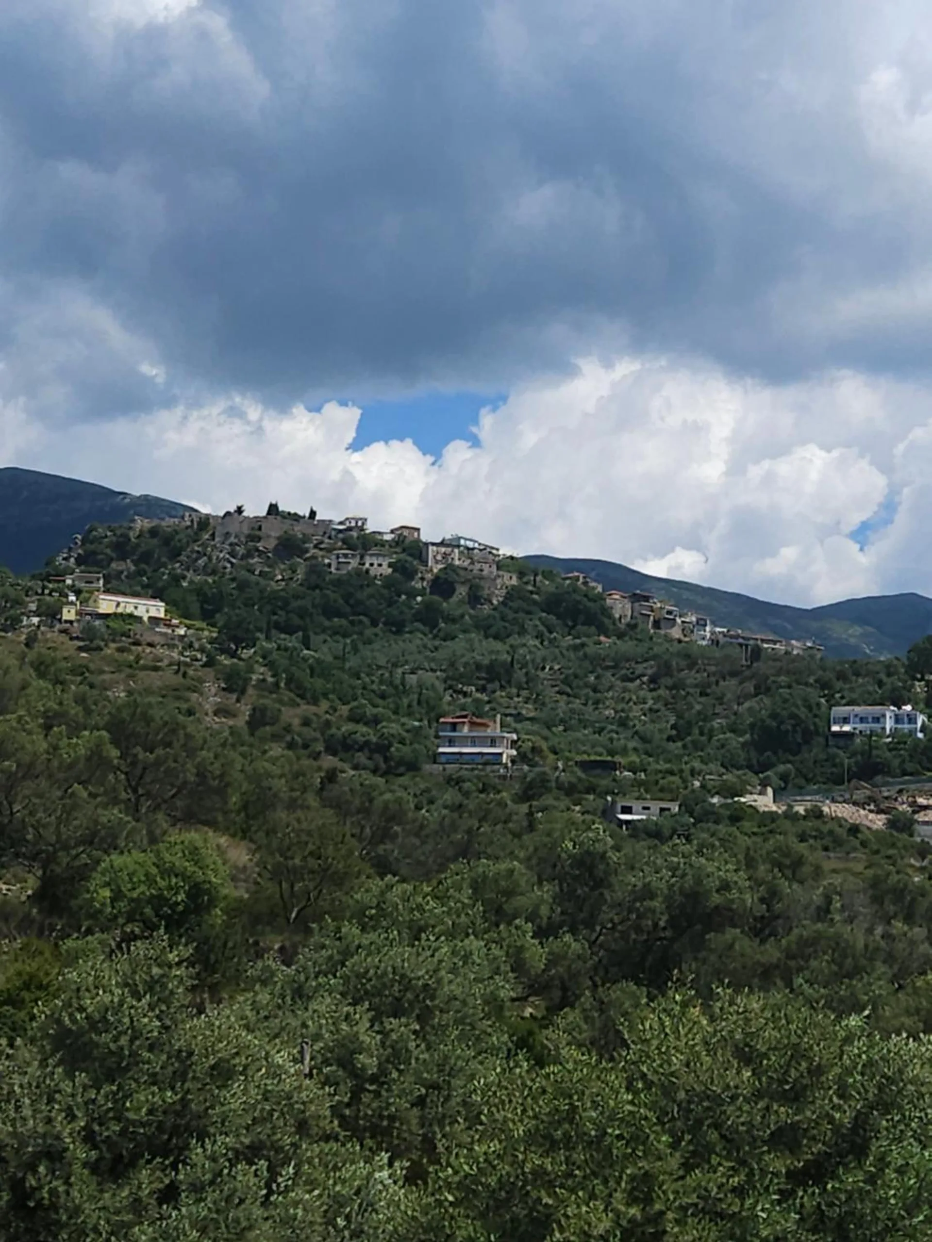 The hill of Himarë Castle with its old houses along the ridge, olive groves below and heavy clouds above